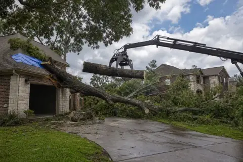 Grapple truck lifting a storm-broken pecan section from a Sugar Land driveway